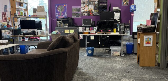 Photo of the GRCGED office with a brown couch, 2 desks, purple walls with posters.